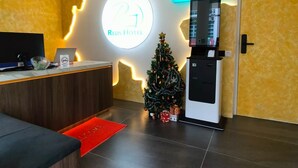 Un espace d’accueil d’hôtel doté d’un terminal en libre-service pour l’enregistrement et le départ, d’un sapin de Noël et d’une enseigne indiquant le nom de l’hôtel, le « Reds Hotel ».