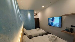 Une chambre d’hôtel avec deux lits, un téléviseur fixé au mur et une étagère avec des articles de toilette.