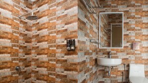 Une salle de bain équipée d’une douche, d’un lavabo et de toilettes, le tout adossé à un mur en pierre orné de motifs.
