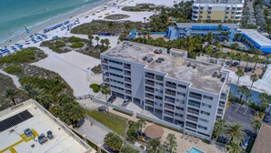 A multi-story hotel with a rooftop pool, adjacent beach, and a parking area. - Location, location! Private Beach, Gulf Views from Balcony, Heated Pool, Siesta Sands with King Bed (Sarasota)