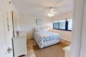 A bedroom with a bed, a nightstand, a dresser, a ceiling fan, and a window.