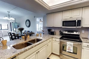 A kitchen with white cabinets, a double sink, a microwave, and a stove. - Siesta Sands Private Beach | Gulf Views | Htd Pool (Sarasota)