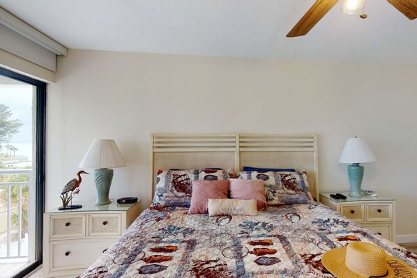 A bedroom with a bed, two bedside tables, a lamp on each table, a window with a view, and a ceiling fan.