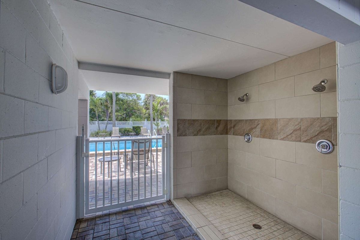 A shower area with a tiled wall and a view of a pool outside.