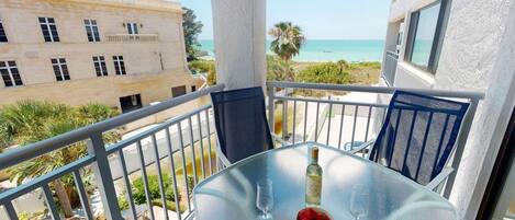 Un balcon avec une table dressée pour deux personnes, donnant sur une plage et des bâtiments.