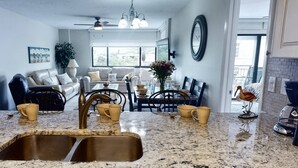 A kitchen with granite countertops, a double sink, and a dining area with a table and chairs. - Location, location! Private Beach, Gulf Views from Balcony, Heated Pool, Siesta Sands with King Bed (Sarasota)