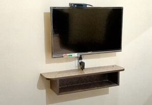 A flat-screen TV mounted on a wall with a shelf below it. - Vairavel Residency (Tiruchendur)