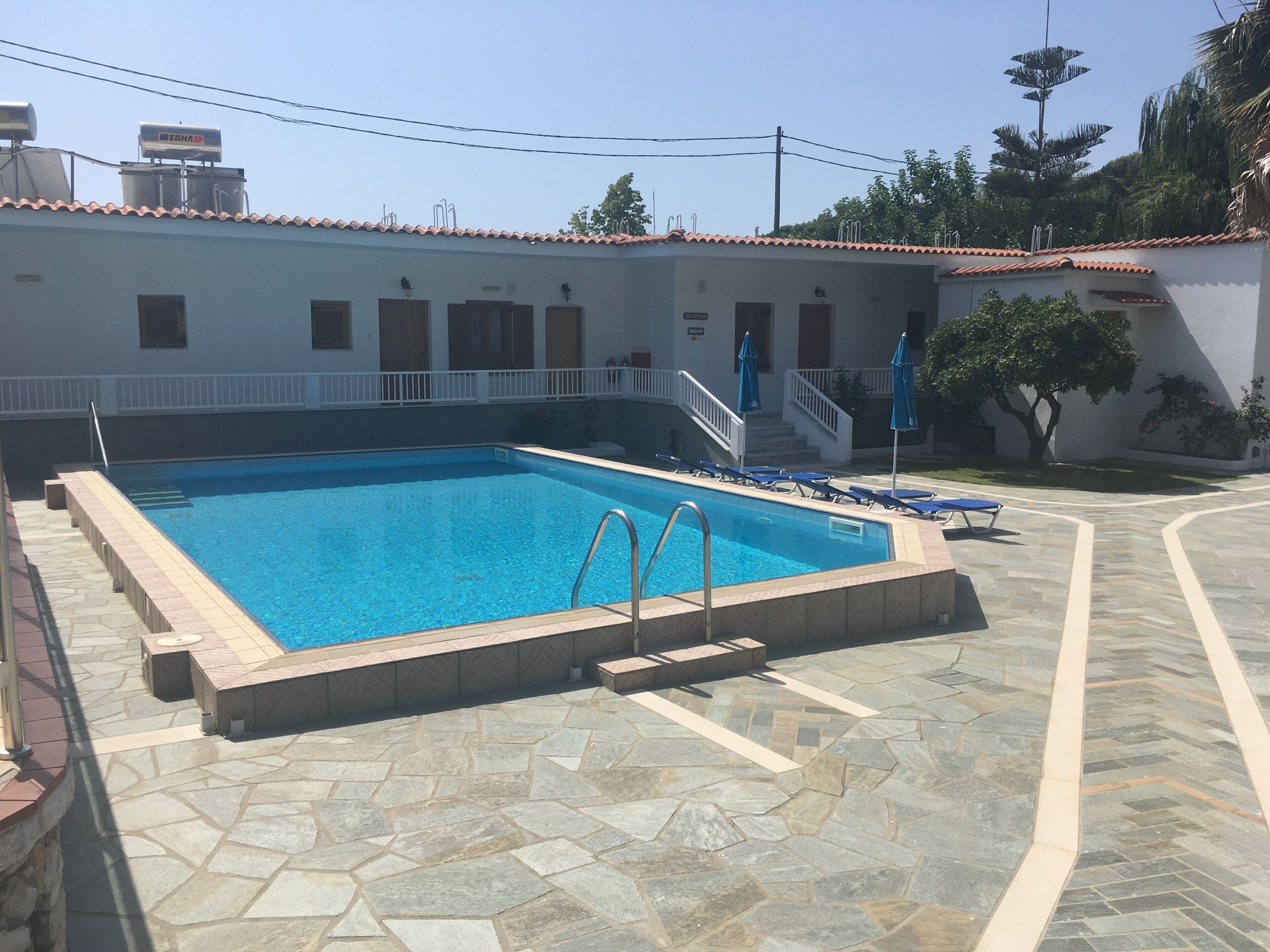 Una piscina con solárium de piedra, una escalera y un edificio blanco con tejado de azulejos.