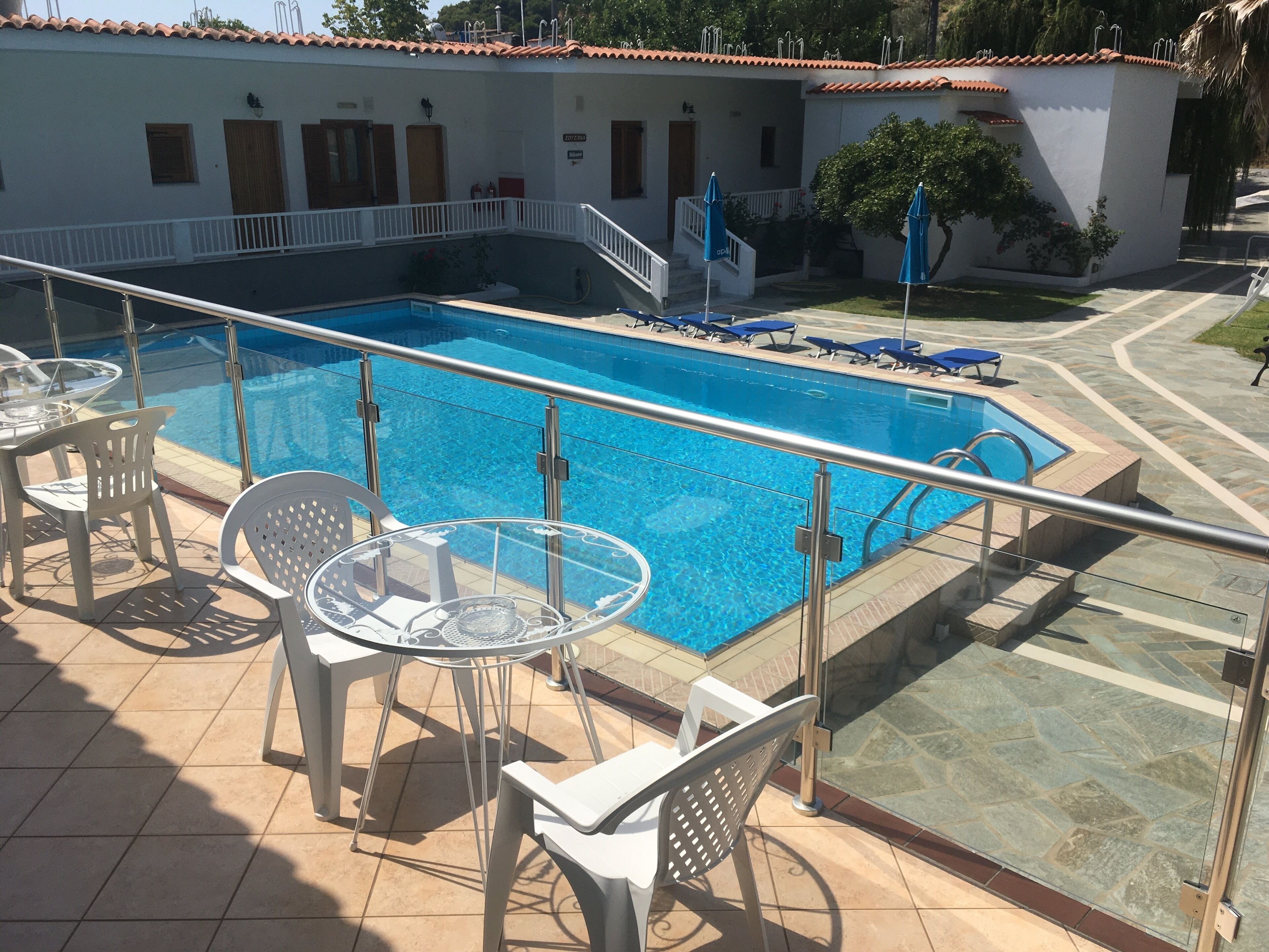A swimming pool with a glass balustrade, surrounded by white plastic chairs and tables.