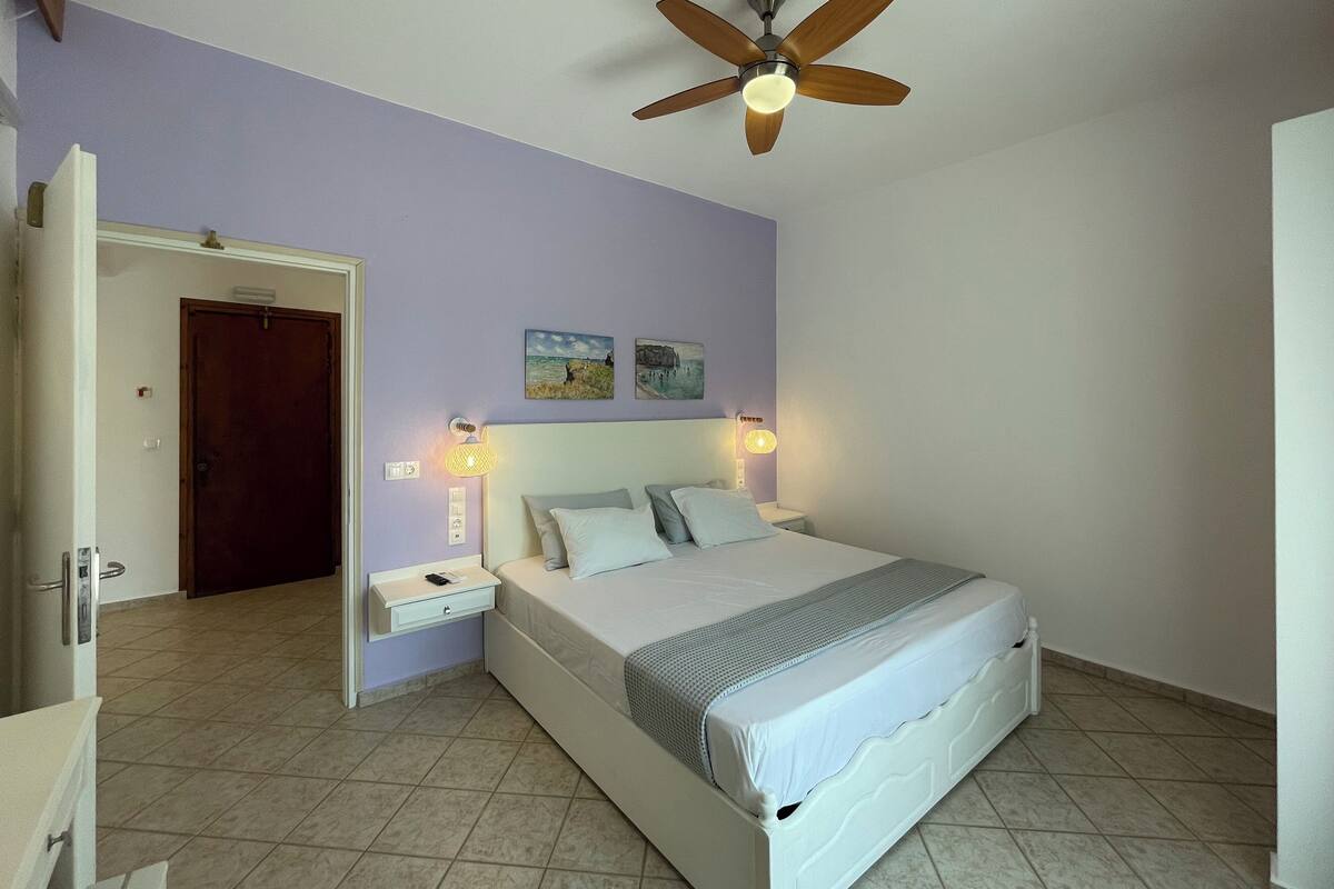 Um quarto com cama, mesas de cabeceira, ventoinha no teto e obras de arte na parede.