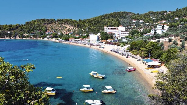 A coastal area with a beach, boats, and buildings on a hillside. - Adult Only - Hotel Suzanna (Skiathos)