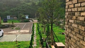 Un balcon donnant sur un paysage verdoyant, une terrasse en bois et un mur en briques.