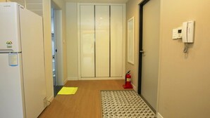 Un couloir avec un réfrigérateur, un extincteur, un tapis à motifs et une porte sur laquelle est fixé un téléphone.