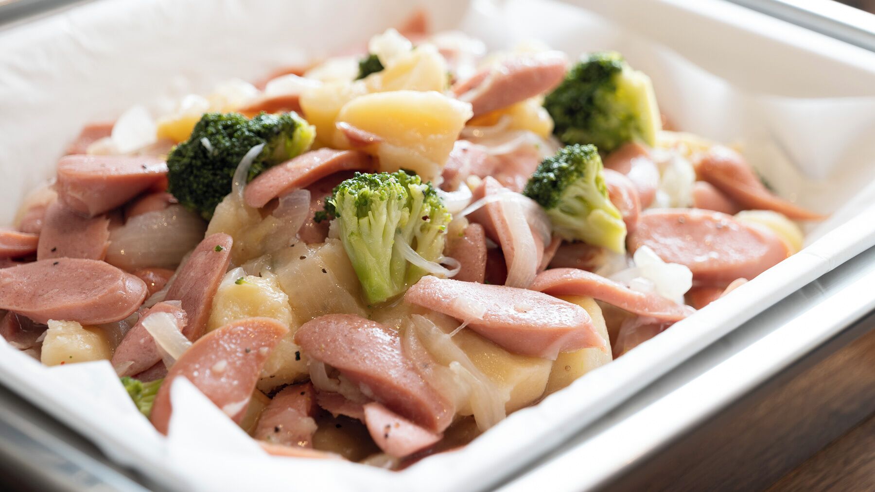 Prato com linguiça fatiada, brócolis e batatas.