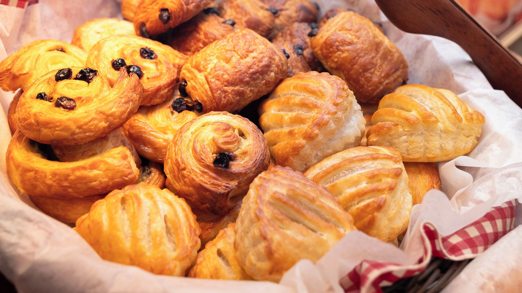 Una variedad de pasteles, incluyendo croissants y hojaldres, dispuestos en una cesta.