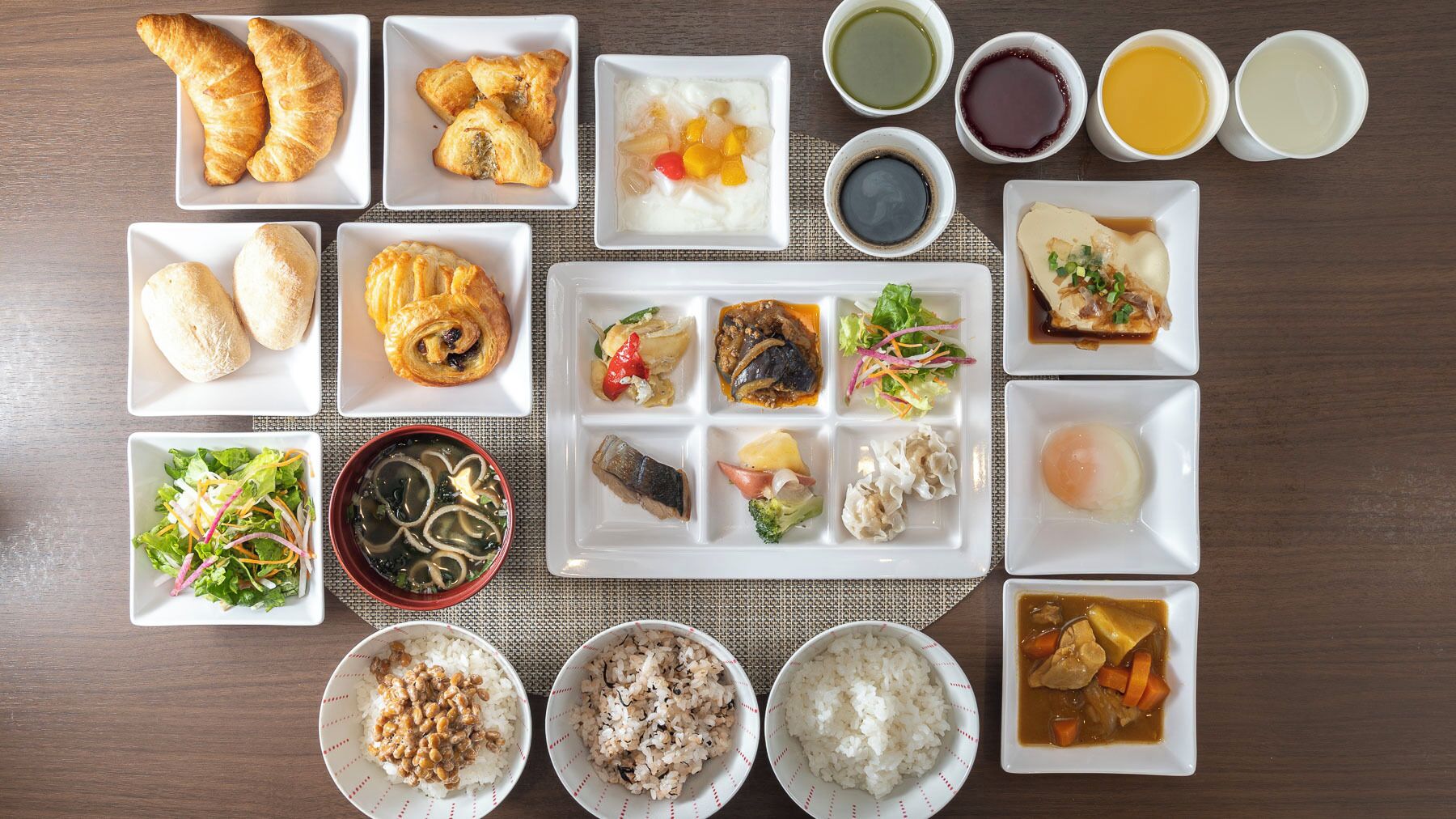 Une variété de plats, notamment des croissants, des bols de riz et une salade, disposés sur une table.