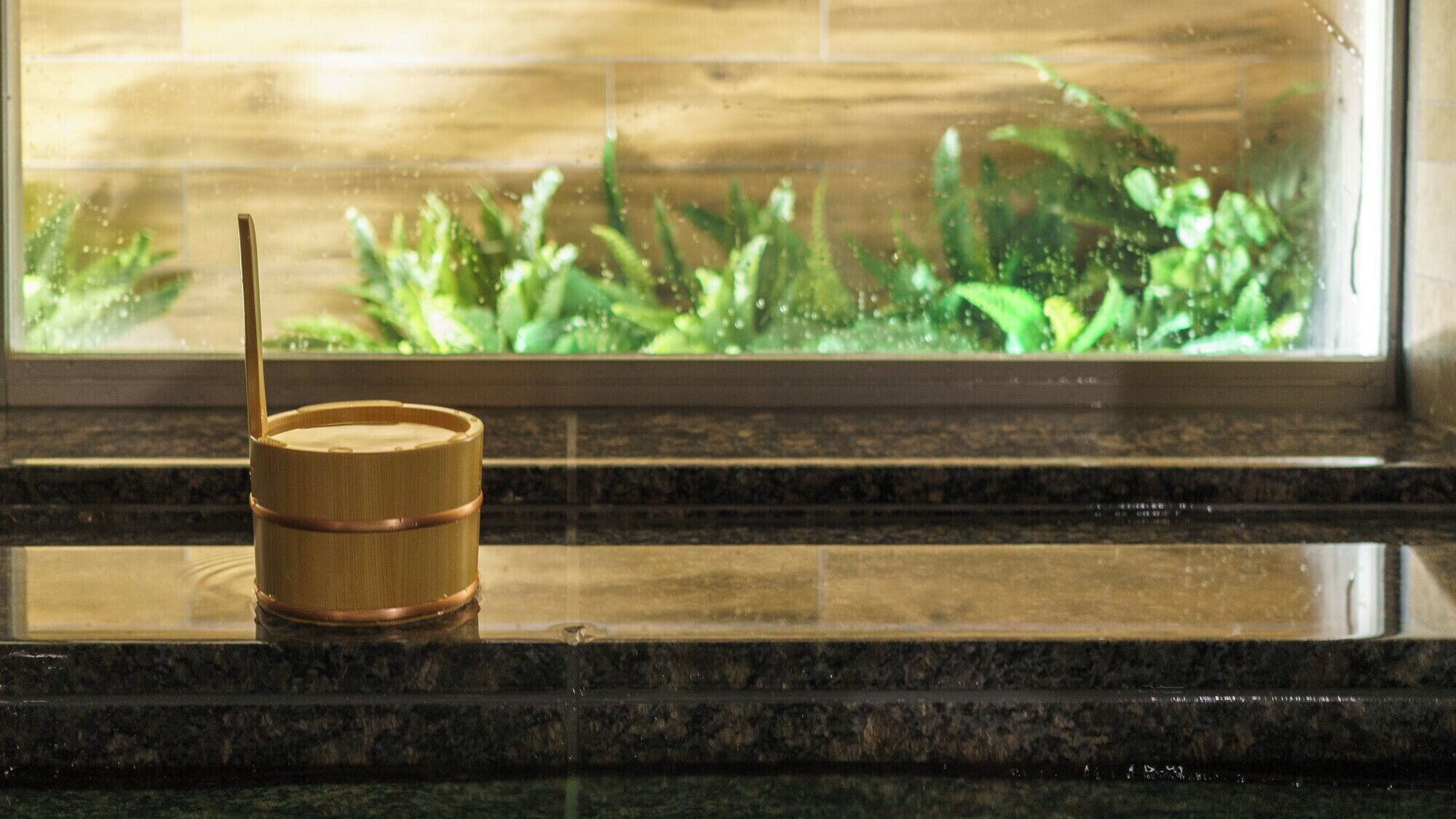 A bamboo water container on a marble countertop near a window with a view of greenery.