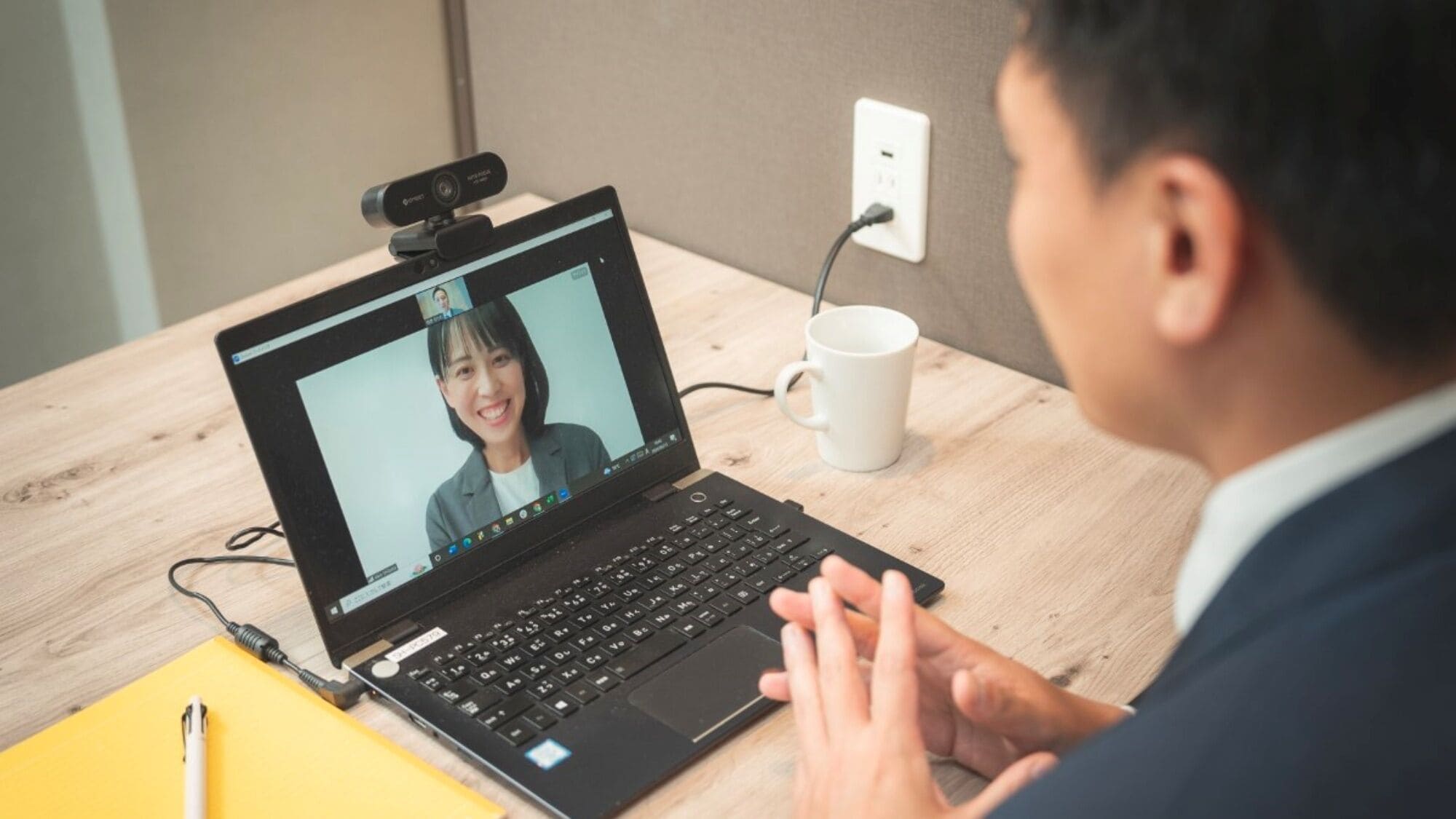 Un ordinateur portable avec une webcam intégrée, une tasse blanche et un dossier jaune, le tout posé sur un bureau en bois.