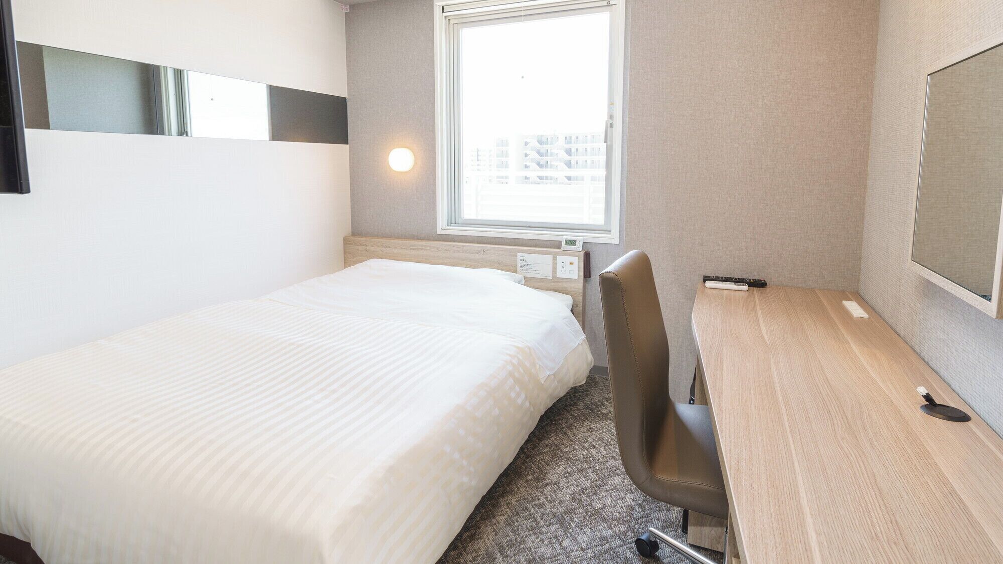 A hotel room with a bed, a desk, a chair, a window, and a wall-mounted TV.