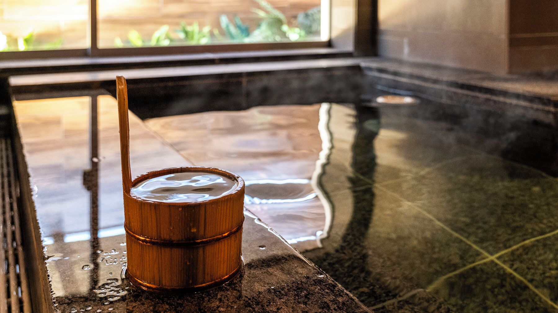 A wooden bucket with a stick on a wet tiled floor near a window.