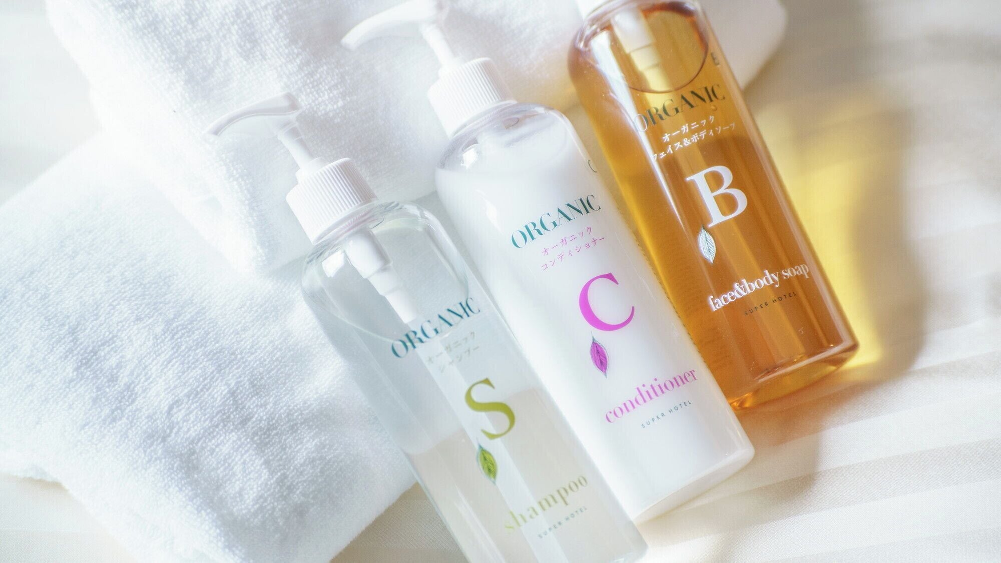 Trois bouteilles de shampoing et d’après-shampoing biologiques posées sur une serviette blanche.