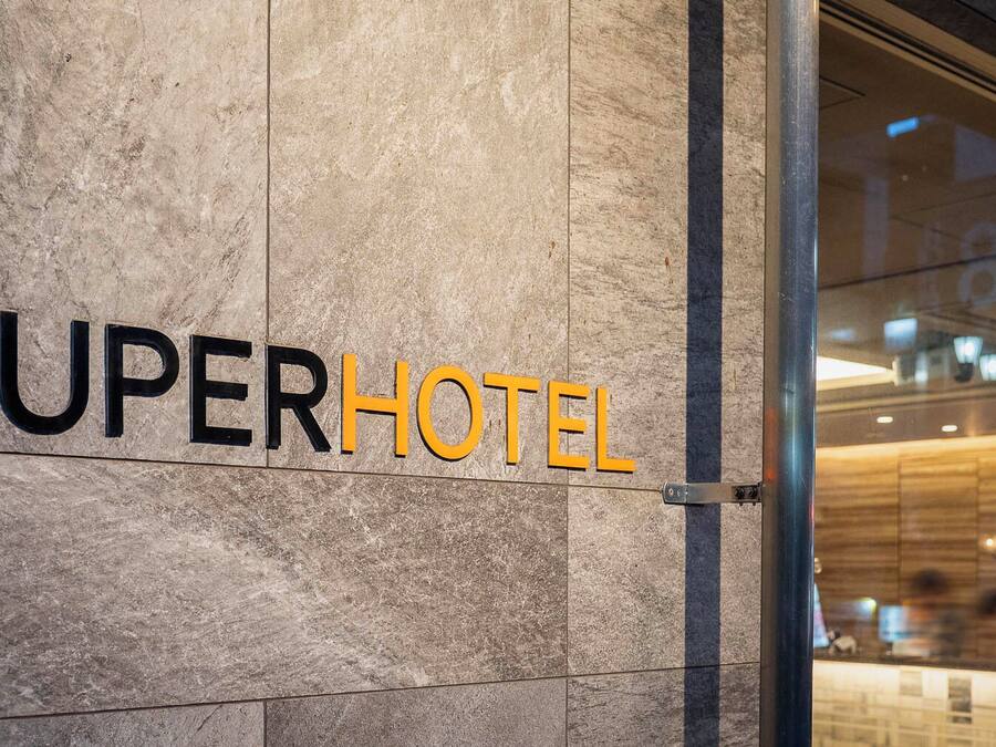 En hotellskylt med namnet ”SUPERHOTEL” skrivet med stora, fetstilta bokstäver på en vägg med en tydlig struktur.