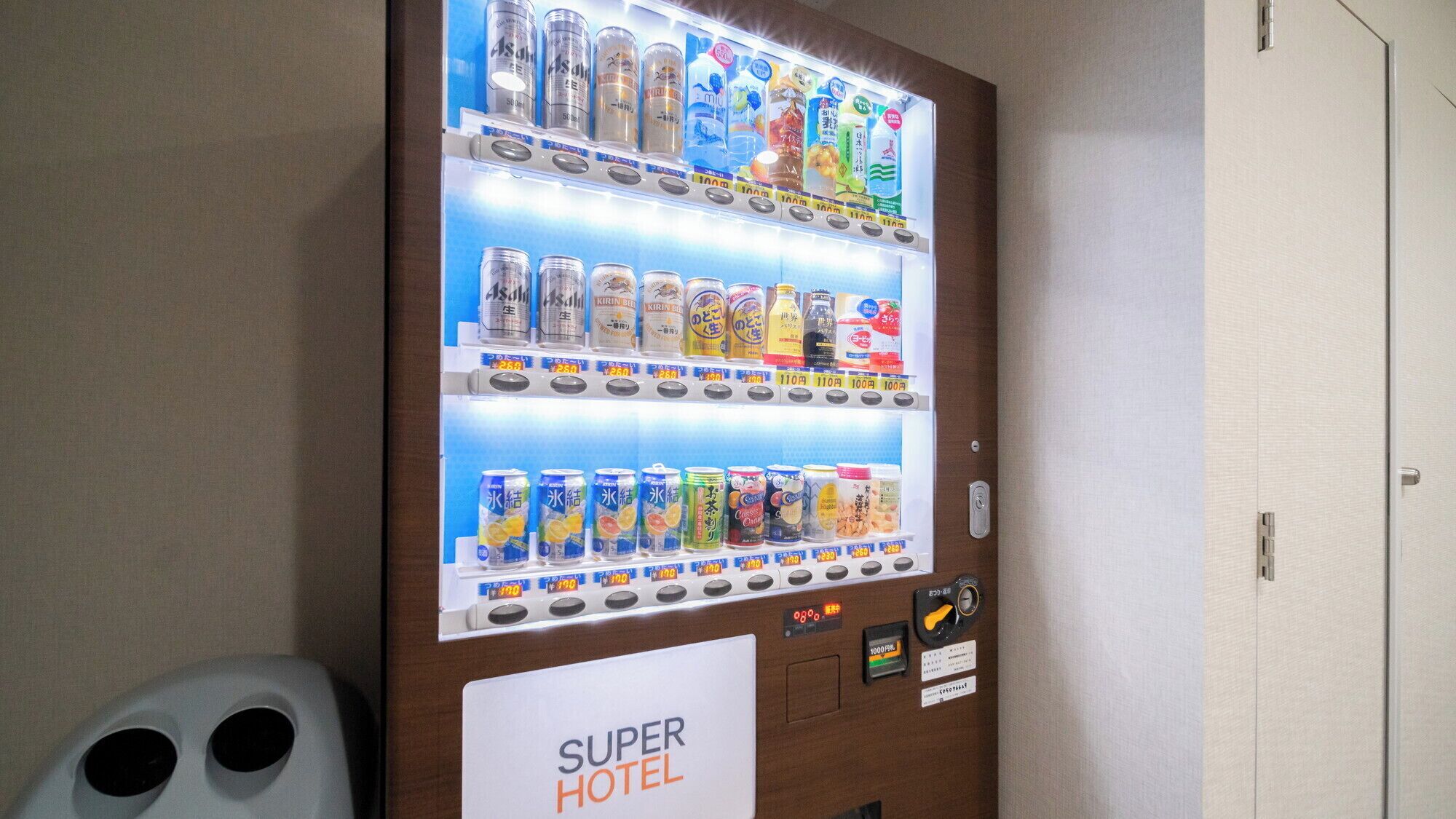 Máquina expendedora con diversas bebidas y aperitivos, etiquetada como "SUPER HOTEL".