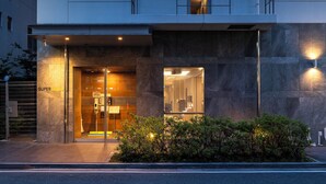 A modern hotel entrance with a glass door, a reception desk, and a well-lit facade.