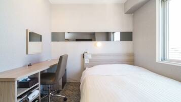 Habitación de hotel con cama, escritorio, silla, espejo y una lámpara en la pared.