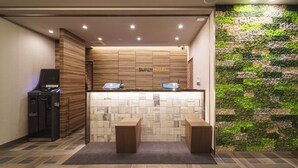 A reception area with a wooden reception desk, two computer monitors, a cash register, and a wall-mounted green wall.