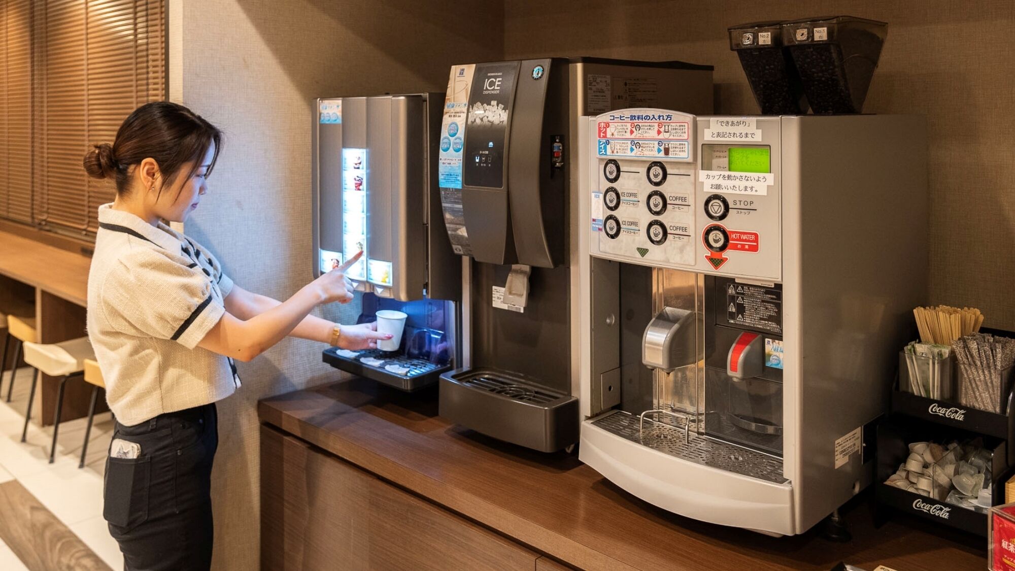 A person operating a coffee machine with multiple dispensers, including options for hot water, coffee, and ice.