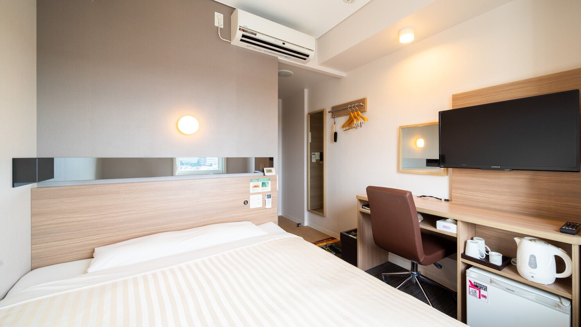 A hotel room with a bed, desk, chair, television, and a small refrigerator.