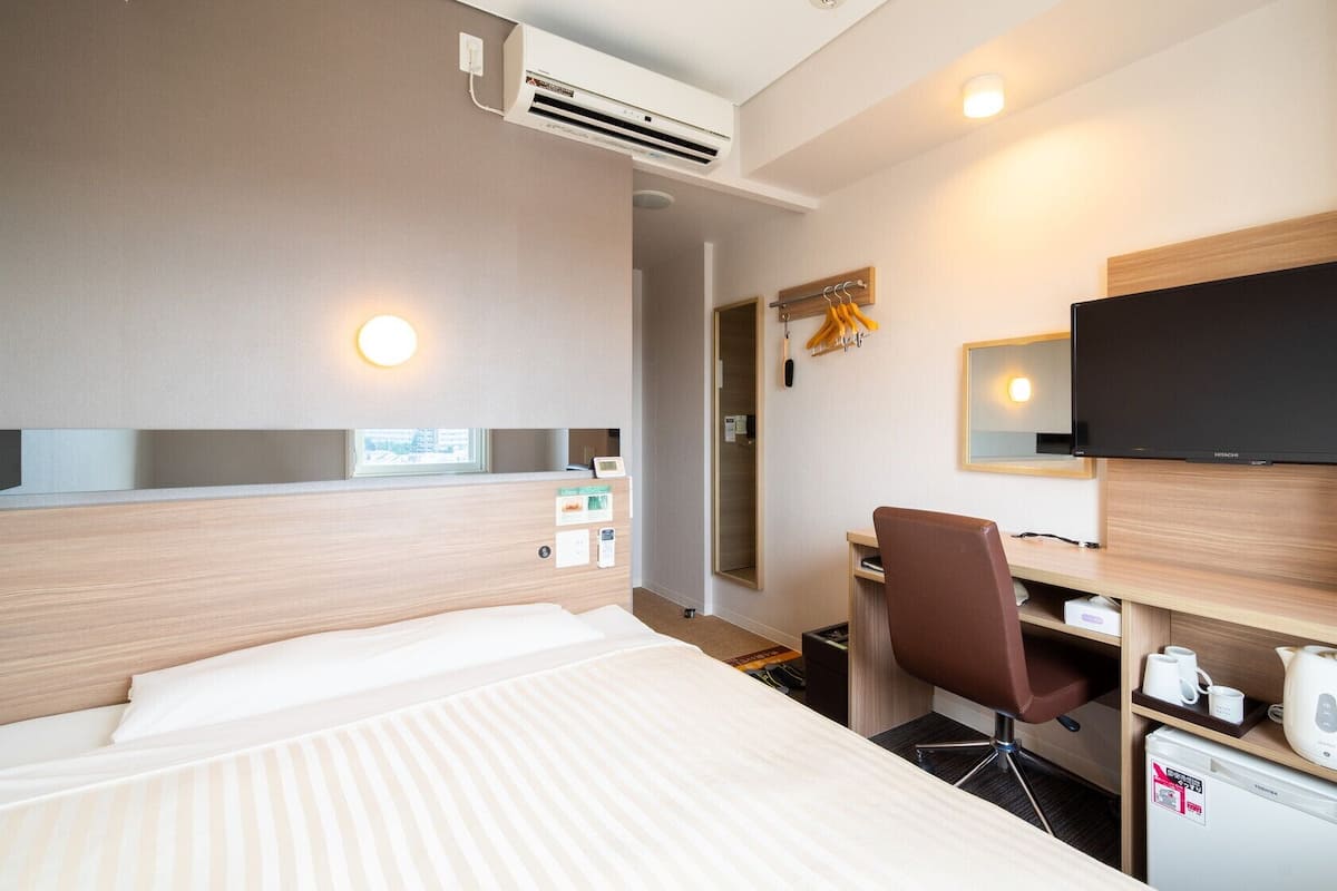 Habitación de hotel con cama, escritorio, silla, televisor y un refrigerador pequeño.
