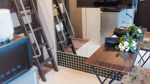A modern kitchen with a built-in TV, a wooden table with a bouquet of flowers, and a ladder leaning against the wall.