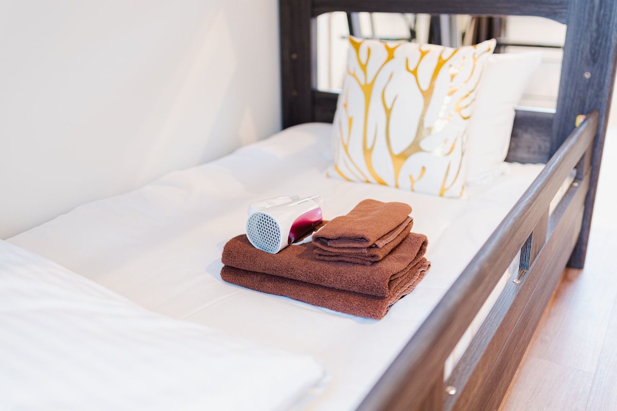 A neatly made bed with a white sheet, a brown towel, and a hairdryer.