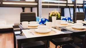 A dining area with tables set for a meal, featuring white plates and cups, a vase with flowers, and a modern interior design.