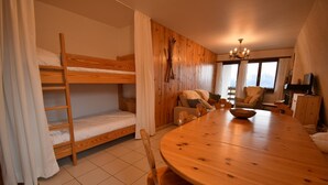 Una habitación con literas, una mesa de comedor de madera, sillas, un candelabro y vistas amplias por las ventanas.