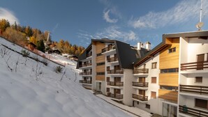 Un edificio moderno de varios pisos con balcones, ubicado en una ladera nevada bajo un cielo despejado.