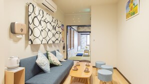 A modern hotel room with a sofa, a wooden table with cups, a small stool, and a wall-mounted air conditioner. - My Home in Tokyo (Tokyo)