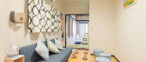 A modern hotel room with a sofa, a wooden table with cups, a small stool, and a wall-mounted air conditioner.