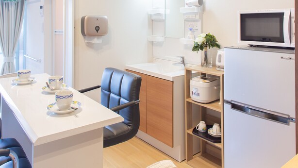 A compact kitchen with a microwave, refrigerator, and a small dining area with chairs and a table. - My Home in Tokyo (Tokyo)