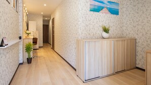 A hallway with patterned wallpaper, a wooden cabinet, a potted plant, and a framed picture on the wall. - My Home in Tokyo (Tokyo)