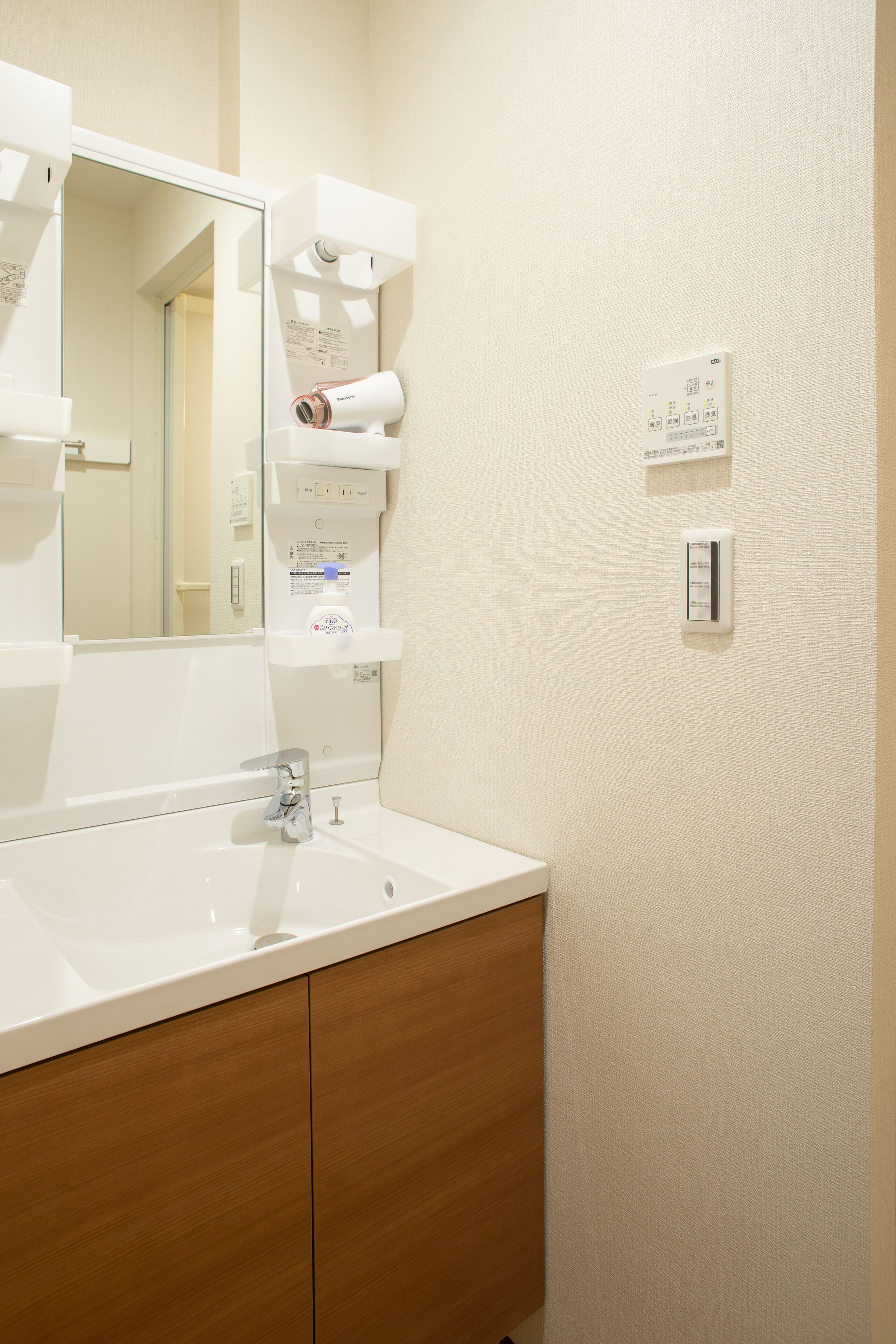 A bathroom with a white sink, a mirror, a towel dispenser, and a wall-mounted light switch.