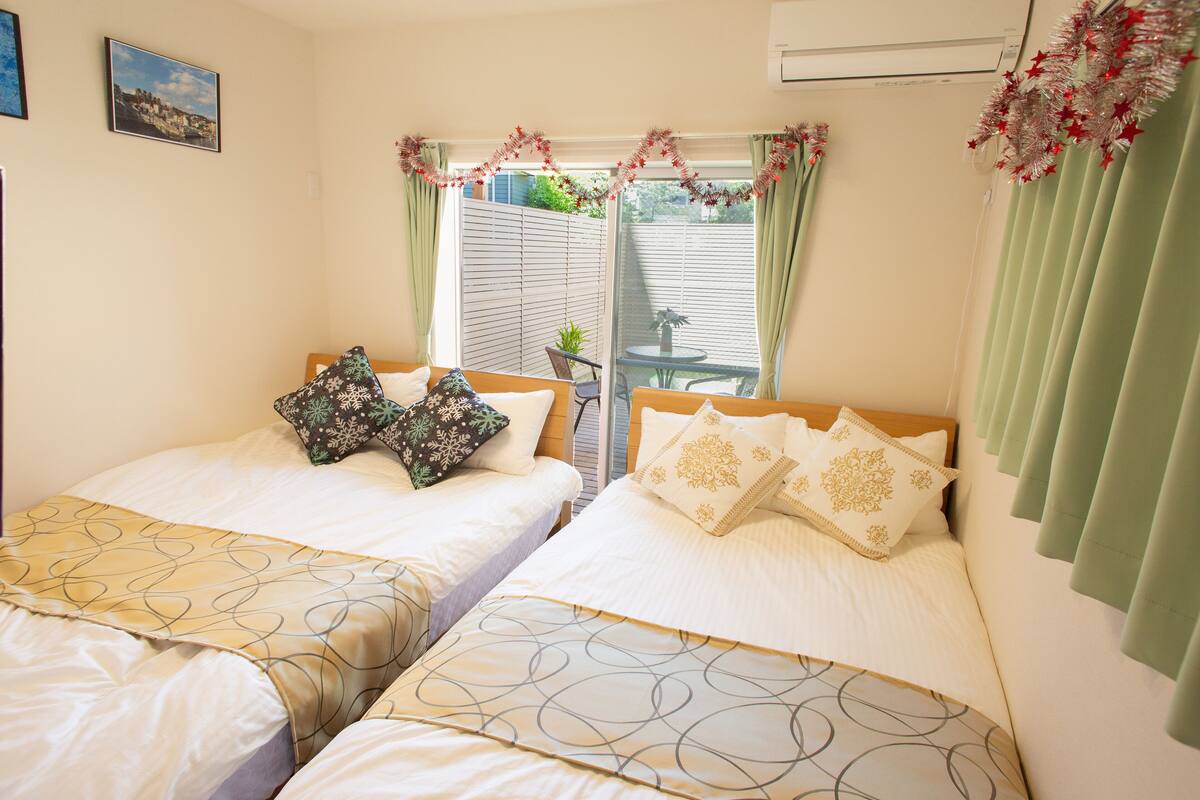A bedroom with two beds, a window with curtains, and a small table with a plant.