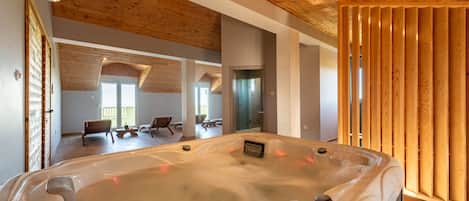 A modern spa room with a wooden ceiling, a hot tub, and a view of a lounge area.