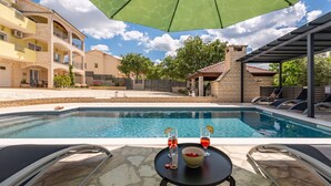 A pool area with a table and chairs, a covered seating area, and a building with balconies. - Villa Balen (Benkovac)