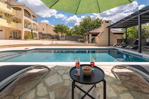 Un espace piscine avec une table et des chaises, un coin salon couvert et un bâtiment doté de balcons.