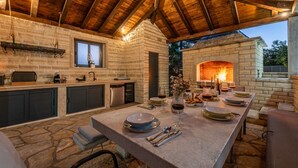 An outdoor kitchen with a stone countertop, built-in cabinets, and a brick fireplace. - Villa Balen (Benkovac)