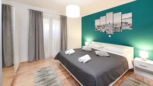 A modern bedroom with a large bed, grey curtains, a teal accent wall, and a cityscape artwork. - Villa Marija (Policnik)
