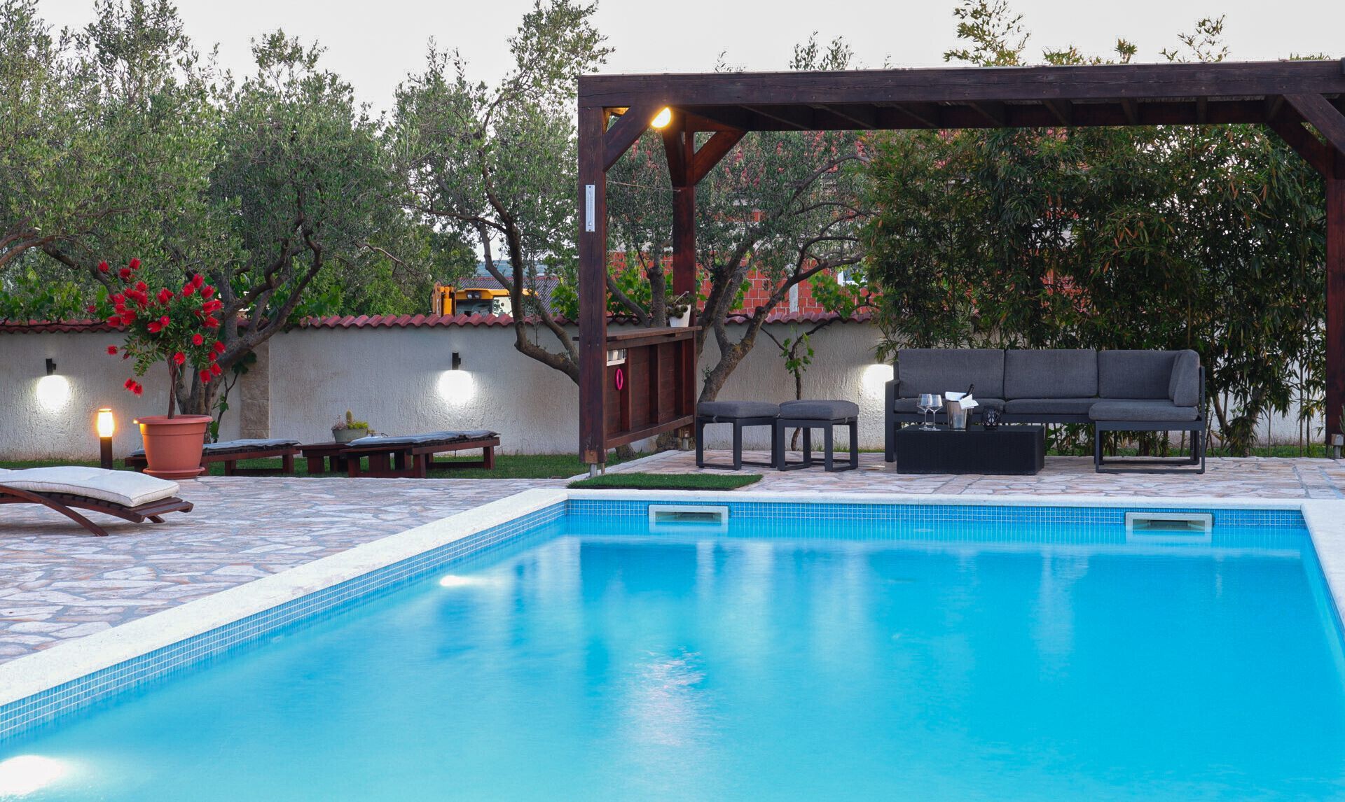 Una piscina con pérgola, mobiliario exterior y plantas en macetas.